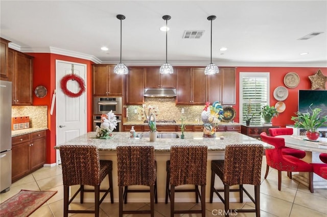 kitchen featuring light stone countertops, light tile patterned floors, decorative light fixtures, and an island with sink