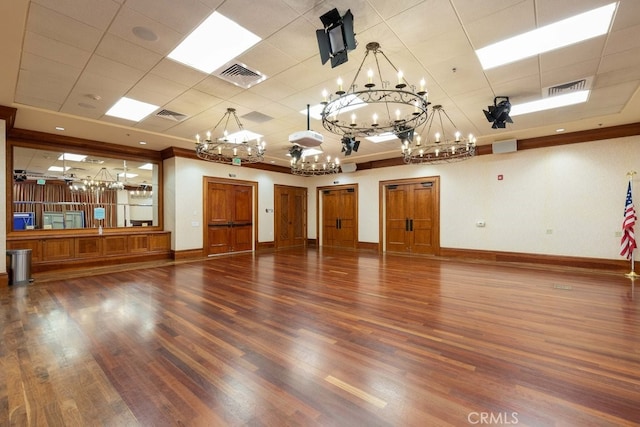 unfurnished room featuring a chandelier, a drop ceiling, and dark wood-type flooring