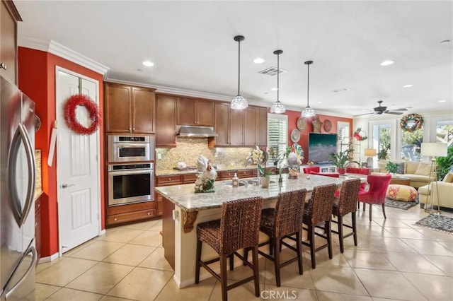 kitchen with appliances with stainless steel finishes, a breakfast bar, ceiling fan, a center island with sink, and hanging light fixtures