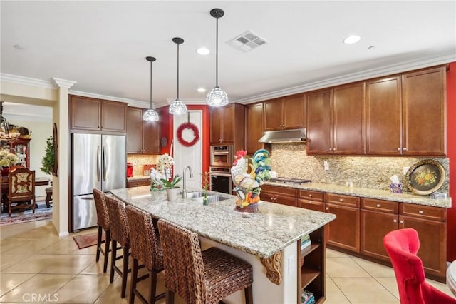 kitchen with light stone counters, sink, stainless steel appliances, and an island with sink