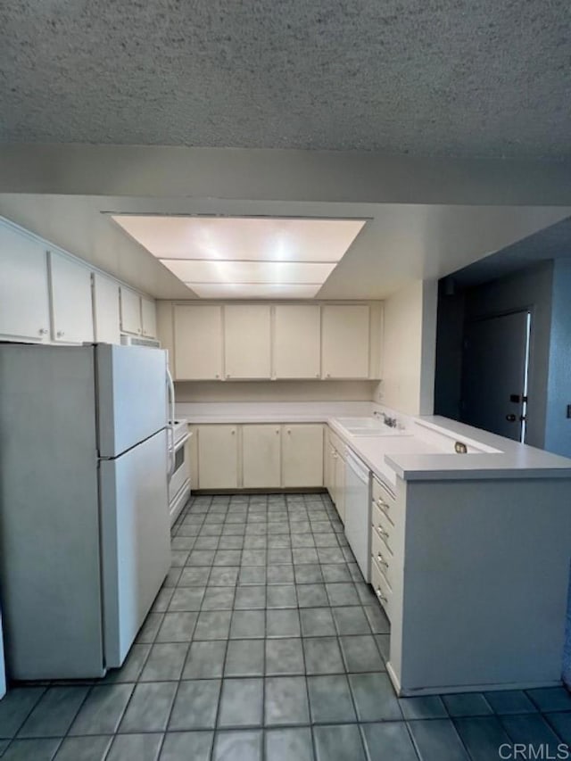 kitchen with white appliances, light tile patterned floors, white cabinets, a peninsula, and light countertops