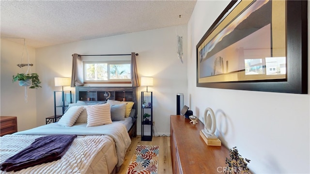 bedroom with a textured ceiling, vaulted ceiling, and light wood-type flooring