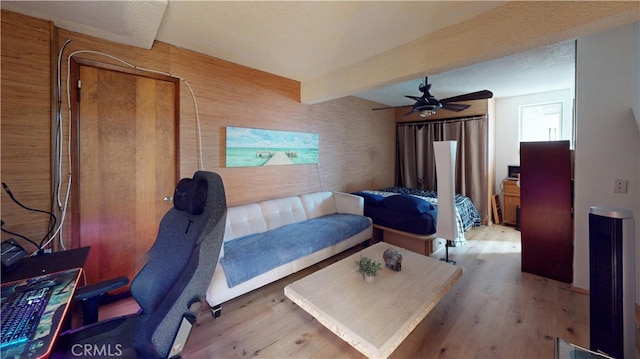 bedroom with beam ceiling, ceiling fan, wood walls, and light wood-type flooring