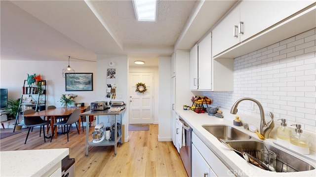 kitchen with dishwasher, sink, light hardwood / wood-style flooring, decorative light fixtures, and white cabinetry