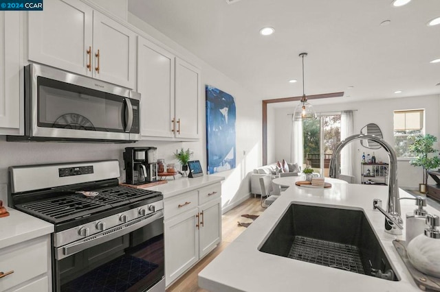 kitchen with white cabinets, hanging light fixtures, sink, light wood-type flooring, and appliances with stainless steel finishes