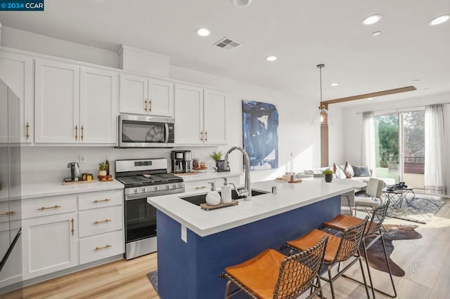 kitchen featuring a kitchen island with sink, a kitchen bar, stainless steel appliances, and hanging light fixtures