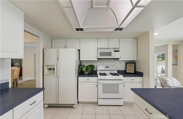 kitchen featuring tasteful backsplash, white cabinets, light tile patterned flooring, and white appliances