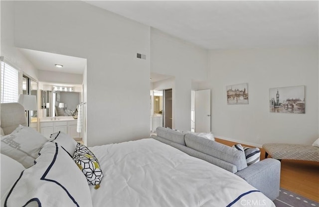 bedroom with wood-type flooring, connected bathroom, and a towering ceiling