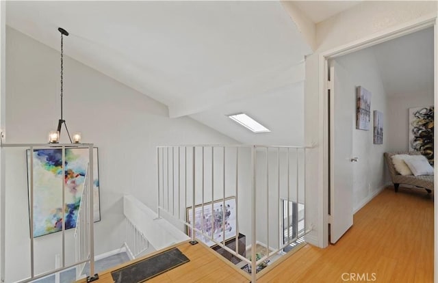 corridor with vaulted ceiling with skylight, hardwood / wood-style floors, and an inviting chandelier