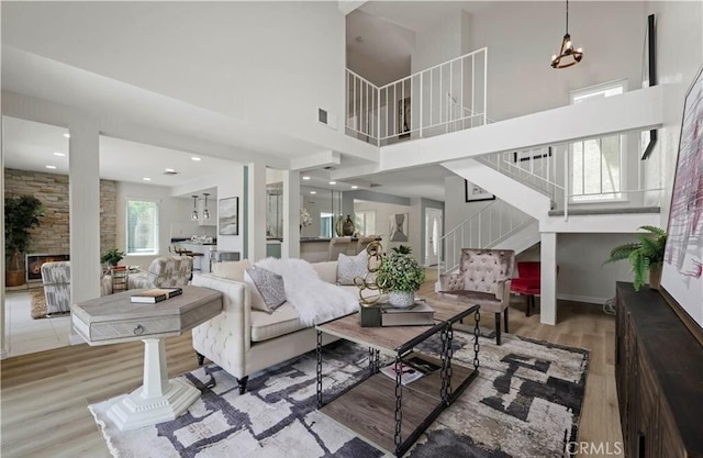 living room featuring a stone fireplace, light hardwood / wood-style floors, a high ceiling, and a notable chandelier