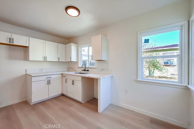 kitchen featuring white cabinets, light wood-type flooring, light stone countertops, and sink