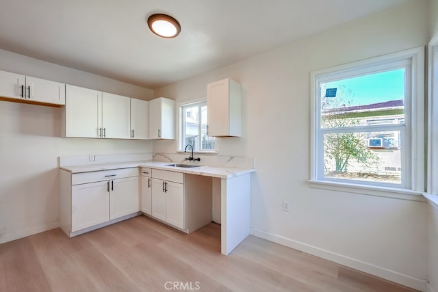 kitchen with white cabinets, a sink, light wood finished floors, and baseboards