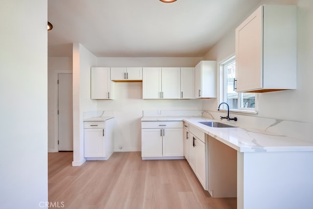 kitchen with white cabinets, light stone countertops, light wood-type flooring, and sink