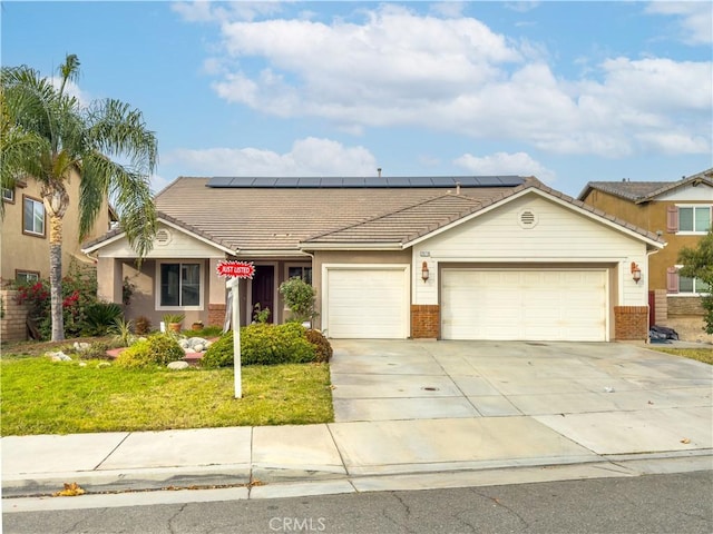 ranch-style home with a garage, a front yard, and solar panels