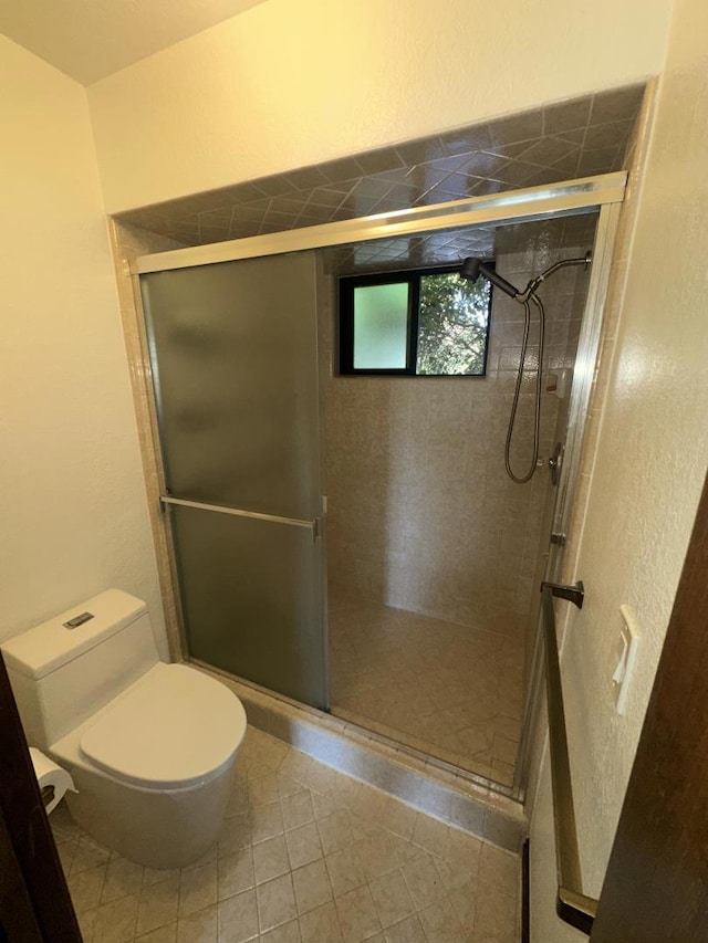 bathroom with tile patterned floors, toilet, and a shower with shower door