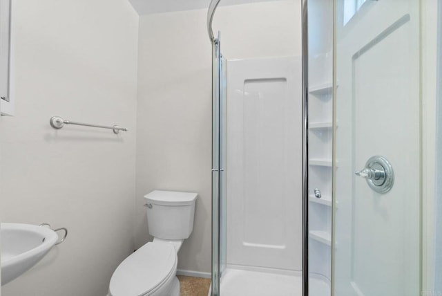 bathroom with a stall shower, toilet, and baseboards