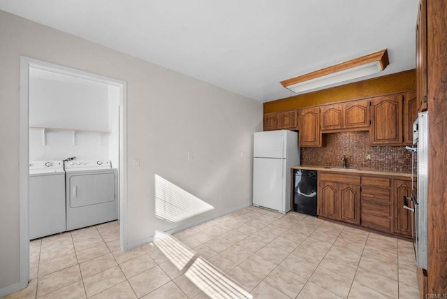 kitchen featuring a sink, black dishwasher, washing machine and dryer, freestanding refrigerator, and brown cabinetry