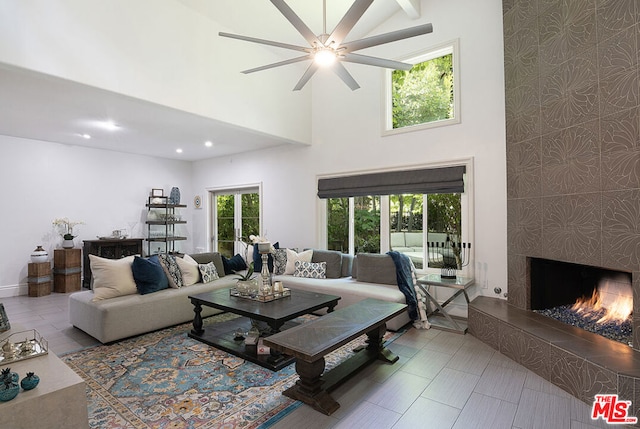 living room featuring a fireplace, ceiling fan, plenty of natural light, and a towering ceiling