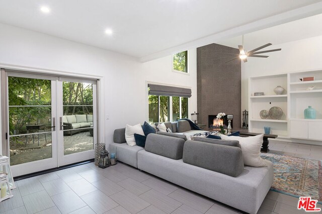 living room featuring vaulted ceiling, ceiling fan, a healthy amount of sunlight, and a tiled fireplace