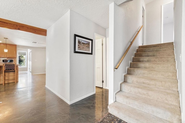 stairway with beamed ceiling, a textured ceiling, and concrete floors