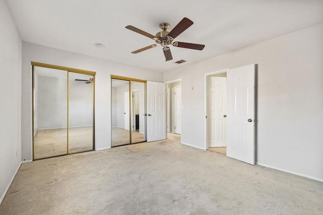 unfurnished bedroom featuring ceiling fan, light colored carpet, and multiple closets