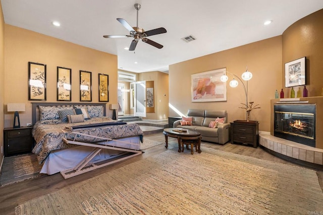 bedroom featuring ceiling fan, light wood-type flooring, and a tile fireplace