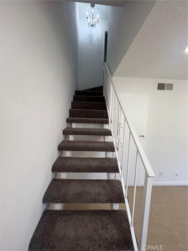 stairs with tile patterned floors, a textured ceiling, and an inviting chandelier