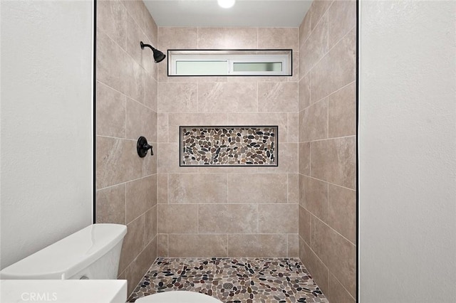 bathroom with a tile shower and toilet