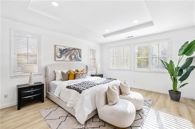 bedroom with a tray ceiling and light hardwood / wood-style flooring