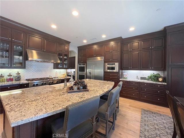 kitchen with backsplash, a kitchen island with sink, light hardwood / wood-style flooring, and stainless steel appliances