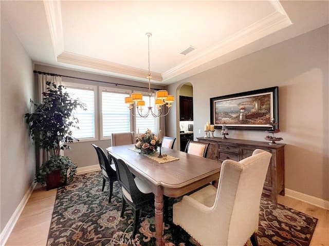 dining space featuring a raised ceiling, an inviting chandelier, ornamental molding, and light wood-type flooring