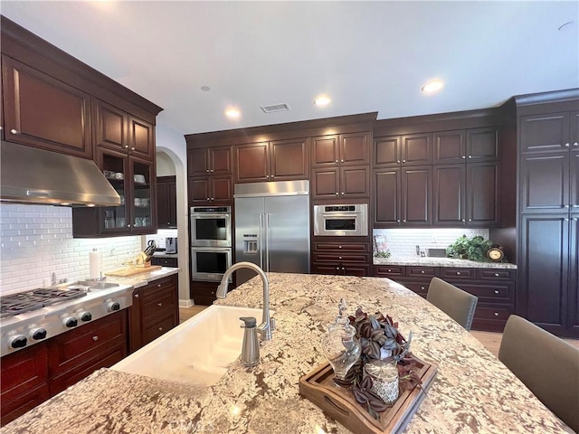 kitchen featuring light stone countertops, sink, a kitchen breakfast bar, backsplash, and appliances with stainless steel finishes