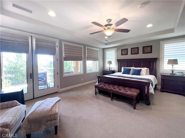 carpeted bedroom with access to outside, multiple windows, a tray ceiling, and ceiling fan