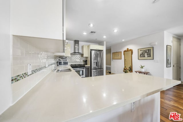 kitchen with sink, kitchen peninsula, stainless steel appliances, and wall chimney range hood