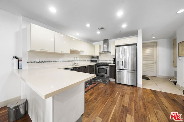 kitchen with kitchen peninsula, appliances with stainless steel finishes, wall chimney exhaust hood, light hardwood / wood-style flooring, and white cabinetry