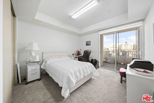 carpeted bedroom with access to exterior and a tray ceiling