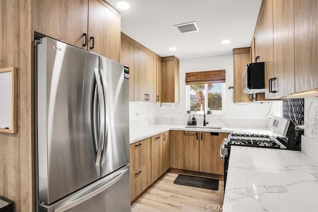 kitchen with light wood-type flooring, white gas range oven, light stone counters, sink, and stainless steel refrigerator