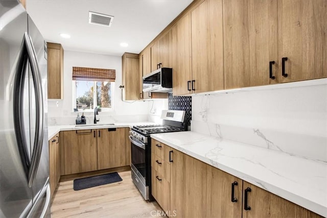 kitchen with light stone countertops, sink, stainless steel appliances, and light hardwood / wood-style flooring