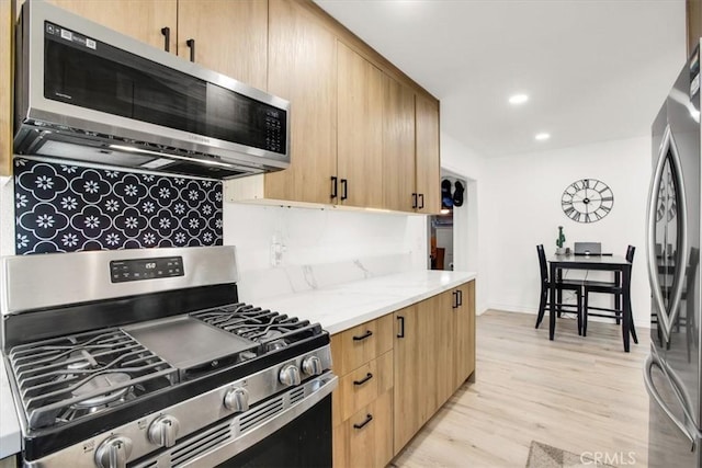 kitchen featuring light brown cabinets, backsplash, light hardwood / wood-style flooring, light stone countertops, and appliances with stainless steel finishes