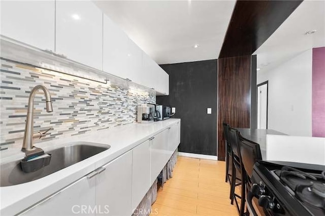 kitchen featuring black gas range, decorative backsplash, white cabinets, and sink