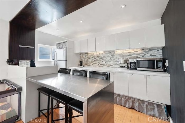 kitchen featuring dishwashing machine, white cabinets, white refrigerator, decorative backsplash, and a breakfast bar area