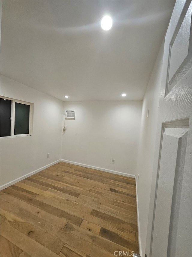 basement featuring recessed lighting, a wall mounted air conditioner, baseboards, and wood finished floors