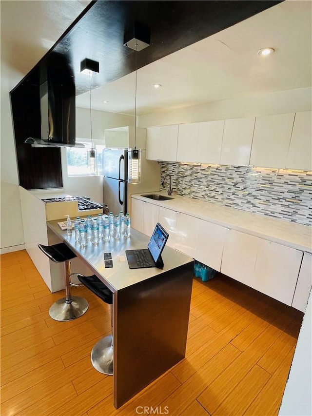 kitchen featuring tasteful backsplash, white cabinets, light wood-style flooring, freestanding refrigerator, and a sink