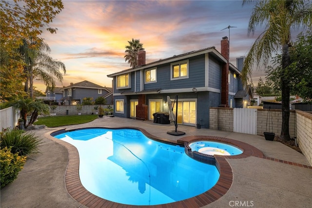 pool at dusk featuring an in ground hot tub and a patio