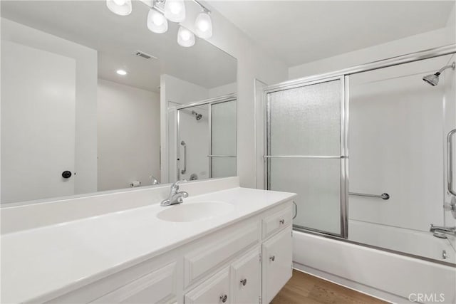 bathroom featuring wood-type flooring, vanity, and bath / shower combo with glass door