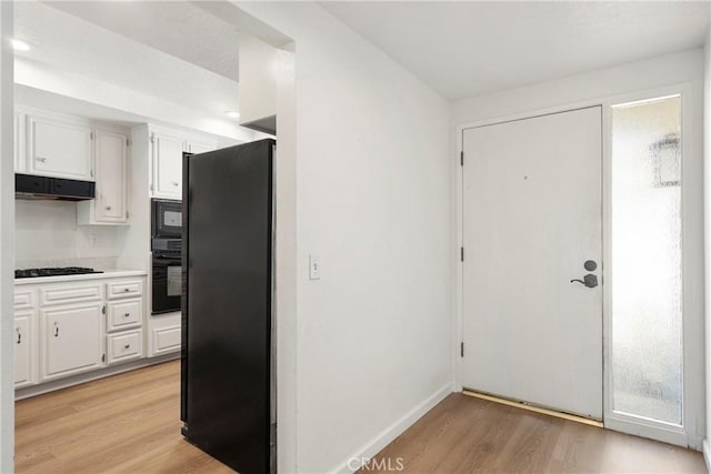 kitchen with ventilation hood, light hardwood / wood-style flooring, white cabinetry, and black appliances