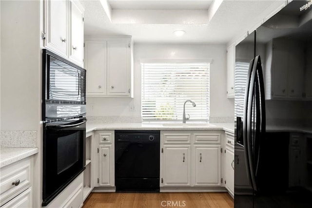 kitchen with black appliances, light hardwood / wood-style floors, white cabinets, and sink