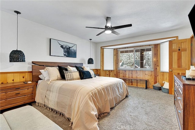 carpeted bedroom with ceiling fan, wood walls, and a textured ceiling