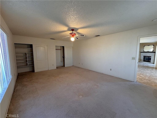 unfurnished bedroom featuring ceiling fan, light colored carpet, a textured ceiling, and a brick fireplace