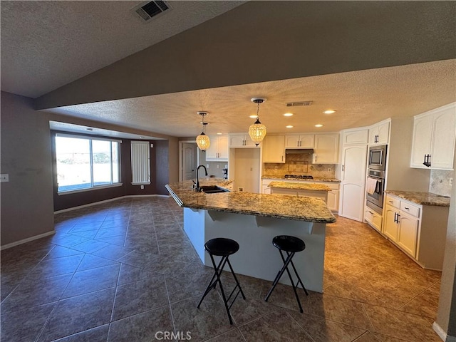 kitchen with vaulted ceiling, sink, a center island with sink, white cabinetry, and hanging light fixtures